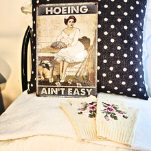  gardening gift set includes gloves and a sign.  the sign is vintage style with a woman in a white frilly dress and says hoeing ain't easy.   the gloves are adorable fingerless crochet in winter white with pink roses and yellow bees.   